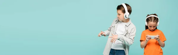 Menina usando smartphone perto menino em fones de ouvido sem fio ouvir música isolada em azul, banner — Fotografia de Stock