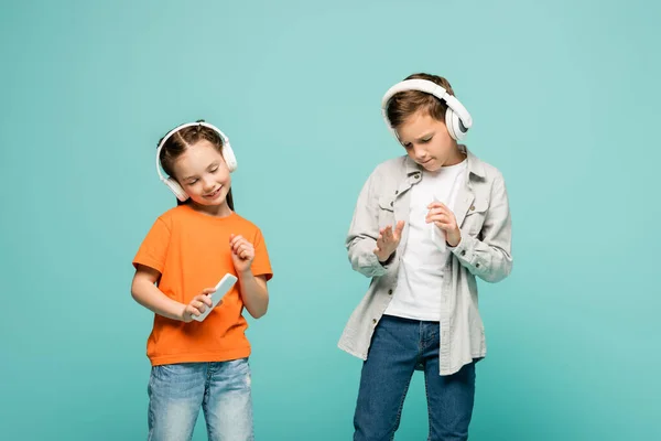 Bambini sorridenti in cuffie wireless ascoltare musica e tenere gli smartphone isolati su blu — Foto stock