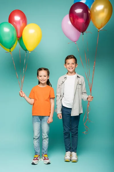 Happy children holding colorful balloons on blue — Stock Photo