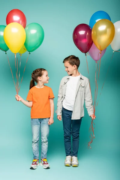 Enfants heureux qui se regardent tout en tenant des ballons colorés sur bleu — Photo de stock