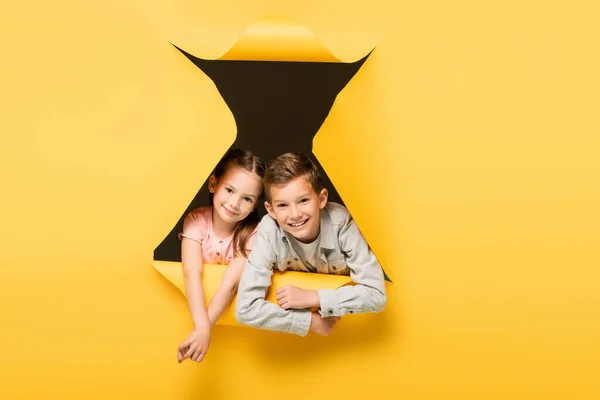 Happy kids looking at camera through hole on yellow background — Stock Photo