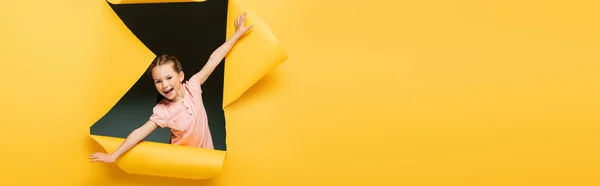 Ragazza eccitata con le mani tese guardando la fotocamera attraverso il buco strappato su sfondo giallo, banner — Foto stock