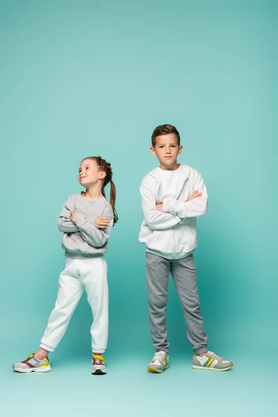 Обиженные мальчик и девочка в спортивной одежде стоят со скрещенными руками на синем — стоковое фото