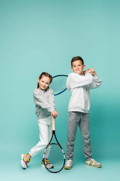 Crianças alegres em sportswear de pé com raquetes de tênis em azul — Fotografia de Stock