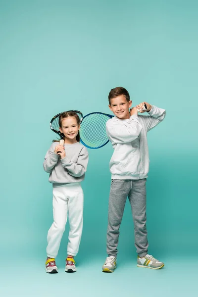 Happy kids in sportswear standing with tennis rackets on blue — Stock Photo