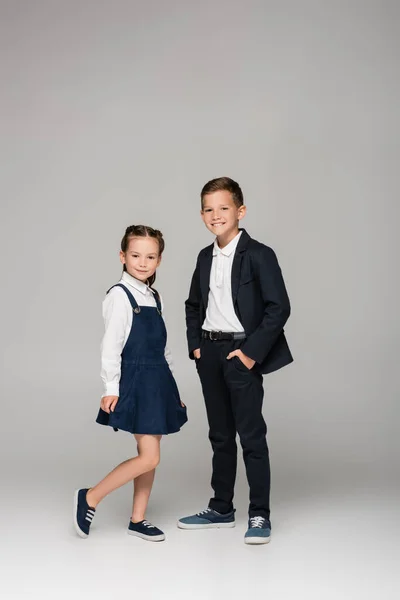 Happy boy standing with hands in pockets near girl in dress on grey — Stock Photo