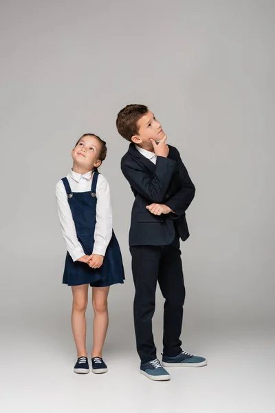 Nachdenkliche Schulkinder in Uniform stehen auf grau — Stockfoto