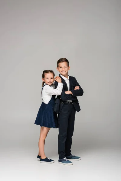 Happy schoolkids in uniform posing and smiling on grey — Stock Photo