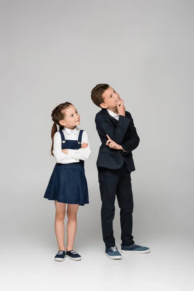 Thoughtful schoolkids in uniform smiling and looking away on grey — Stock Photo