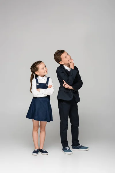 Escolares pensativos em uniforme sorrindo e olhando para o cinza — Fotografia de Stock