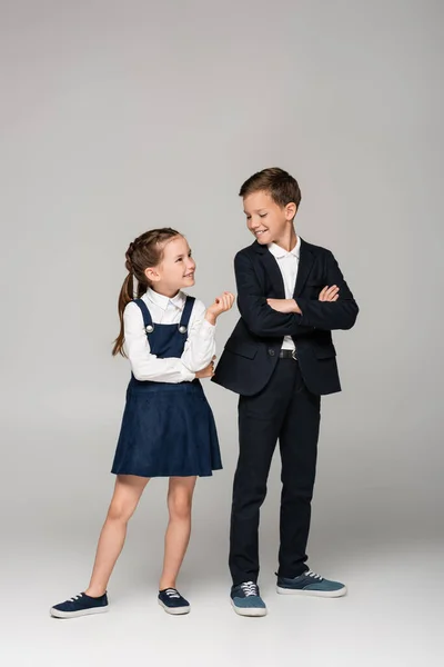 Happy schoolchildren looking at each other while posing on grey — Stock Photo