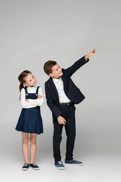 Girl in dress standing with crossed arms near boy pointing with finger on grey — Stock Photo