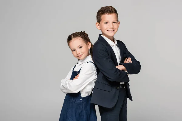 Glückliche Schulkinder in Uniform posieren mit verschränkten Armen in Grau — Stockfoto