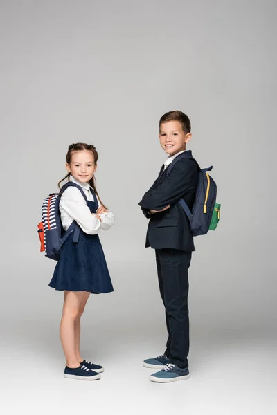 Schoolchildren with backpacks posing with crossed arms on grey — Stock Photo