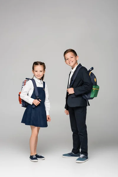 Schoolchildren with backpacks standing and smiling on grey — Stock Photo