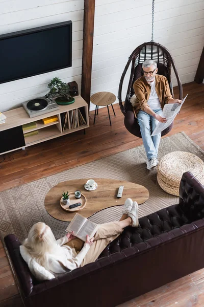 Mann zeigt mit Buch im Wohnzimmer auf Zeitung neben Seniorin — Stockfoto