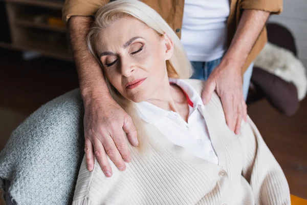 Mann umarmt Seniorin zu Hause mit geschlossenen Augen — Stockfoto