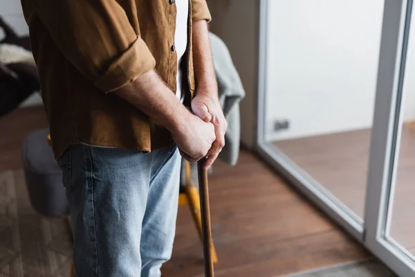 Vue recadrée d'un homme âgé tenant une béquille à la maison — Photo de stock