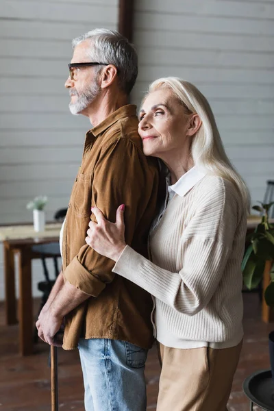 Lächelnde Frau umarmt älteren Mann mit Krücke zu Hause — Stockfoto