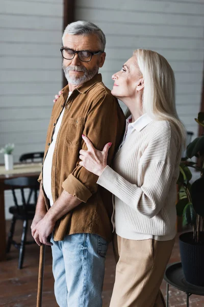 Smiling woman embracing husband with crutch at home — Stock Photo