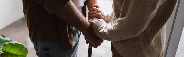 Vista cortada de mulher idosa segurando as mãos do marido com muleta, bandeira — Fotografia de Stock