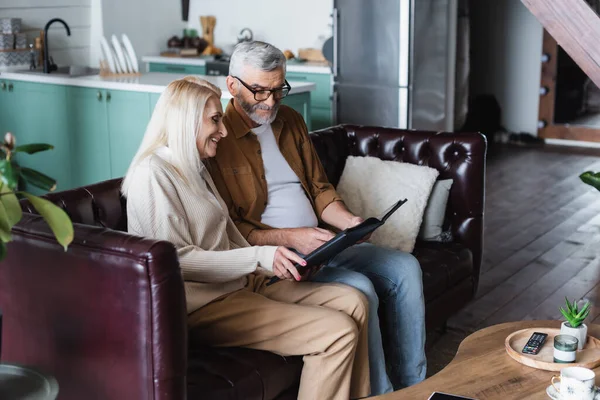 Lächelnde Frau hält Fotoalbum mit Ehemann auf Couch — Stockfoto