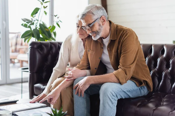 Elderly couple looking at photo album in living room — Stock Photo