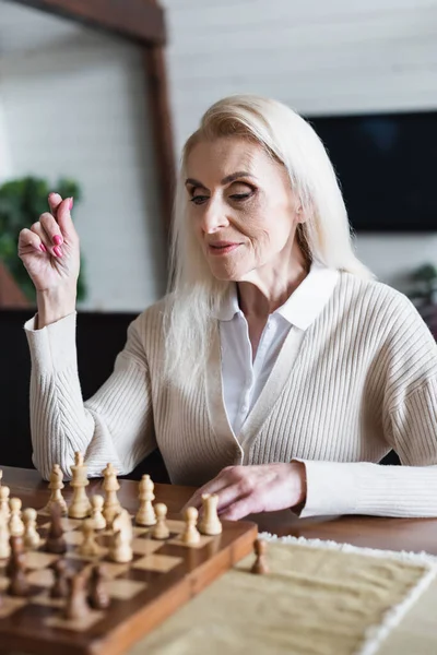 Mujer mayor sentada cerca de ajedrez borroso a bordo - foto de stock