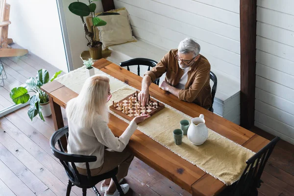 Femme âgée pointant avec la main près du mari et des échecs sur la table — Photo de stock