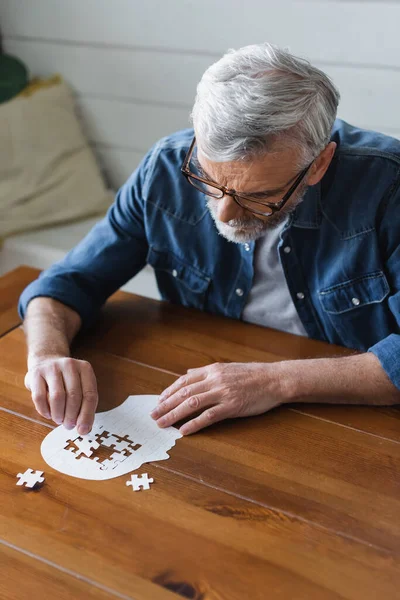 Uomo anziano con demenza tenendo puzzle sul tavolo — Foto stock