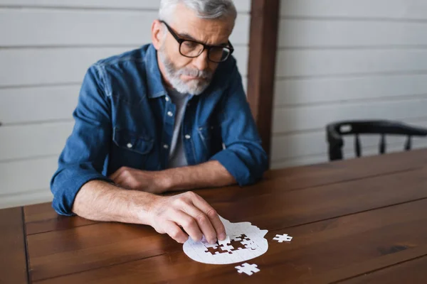 Jigsaw near blurred senior man in eyeglasses at table — Stock Photo