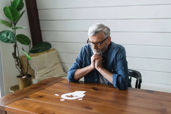 Umsichtiger Senior schaut auf Puzzle auf Tisch — Stockfoto