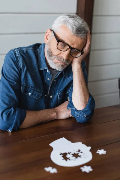 Triste hombre mayor con demencia mirando rompecabezas en la mesa - foto de stock