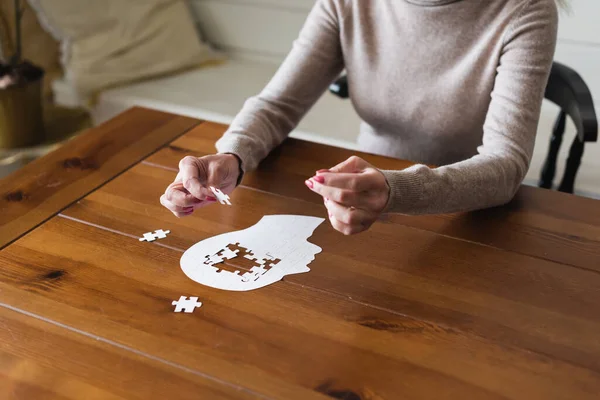 Vista recortada de la mujer mayor sosteniendo rompecabezas cerca de la mesa - foto de stock
