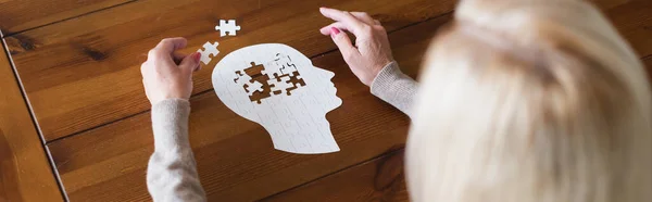 Overhead view of blurred woman holding part of jigsaw on table, banner — Stock Photo