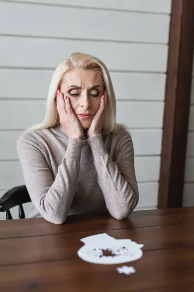 Traurige ältere Frau mit Demenz sitzt neben verschwommenem Puzzle auf Tisch — Stockfoto