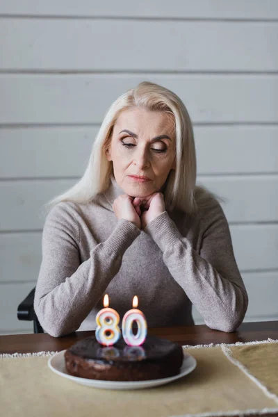 Donna anziana guardando la torta di compleanno offuscata sul tavolo — Foto stock