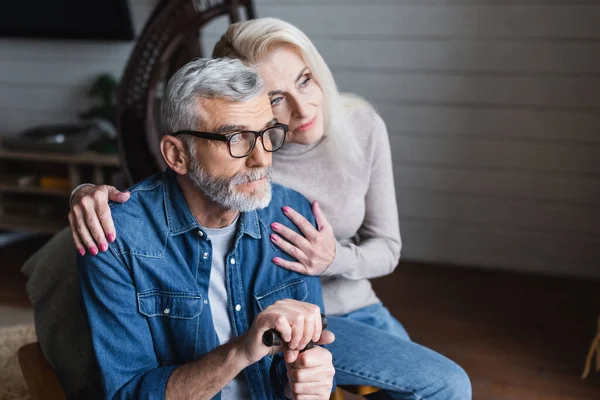 Vorsichtige Frau auf verschwommenem Hintergrund umarmt älteren Mann mit Krücke — Stockfoto