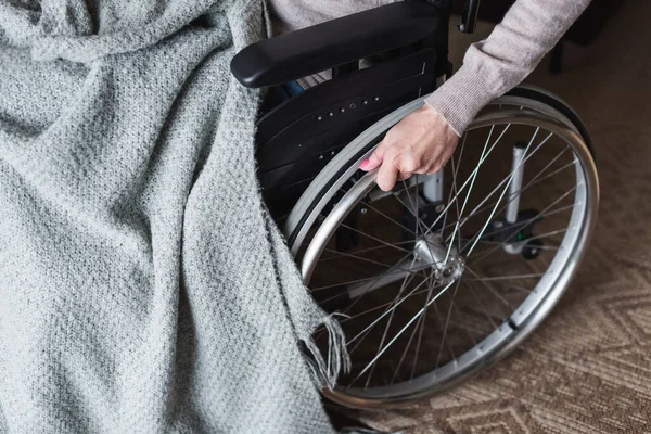 Vista ritagliata della donna anziana che tiene la ruota della sedia a rotelle a casa — Foto stock