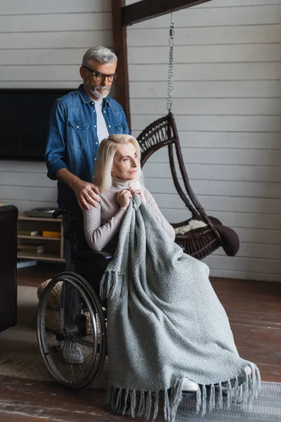 Anciano abrazando esposa en silla de ruedas con manta - foto de stock