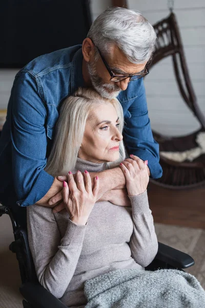 Careful man hugging wife in wheelchair at home — Stock Photo