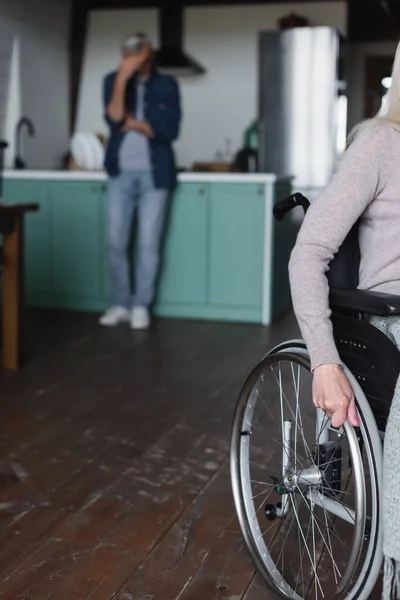 Woman in wheelchair near blurred husband in kitchen — Stock Photo