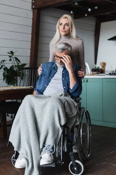 Mujer cuidadosa abrazando al hombre triste en silla de ruedas en casa - foto de stock