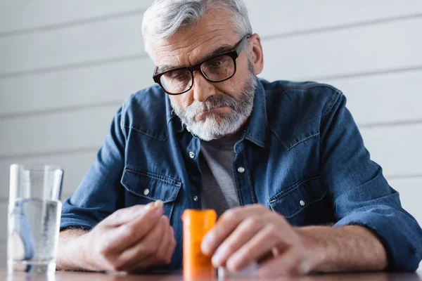 Elderly man holding jar and pills near water on blurred foreground — Stock Photo