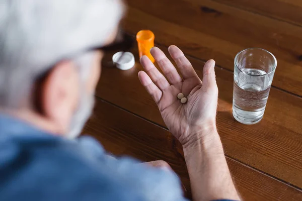 Размытый человек с таблетками на руках возле банки и стакана воды — стоковое фото
