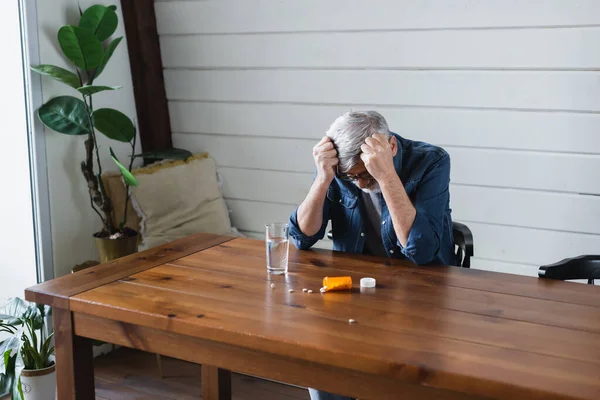 Самотній чоловік сидить біля розкиданих таблеток і води вдома — стокове фото
