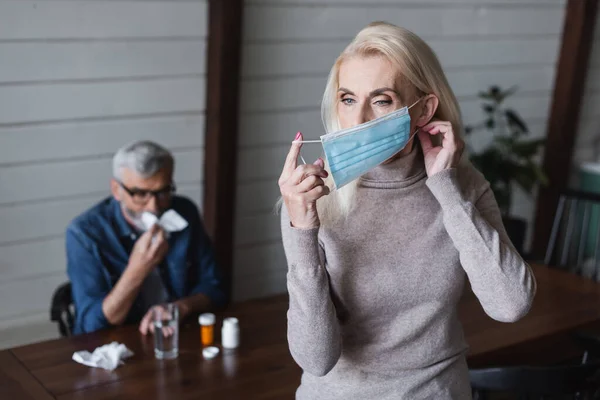 Woman wearing medical mask near blurred husband with napkin and pills — Stock Photo