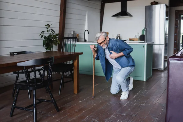 Sick man with crutch holding hand on chest while falling on floor — Stock Photo