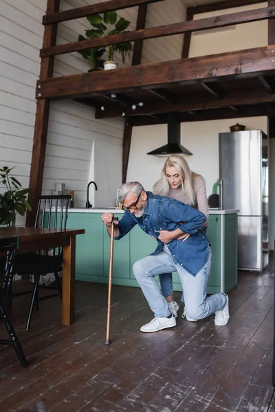 Senior woman helping sick husband with crutch at home — Stock Photo