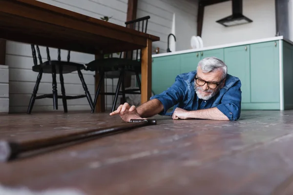 Surface level of disabled senior man taking crutch while lying on floor at home — Stock Photo